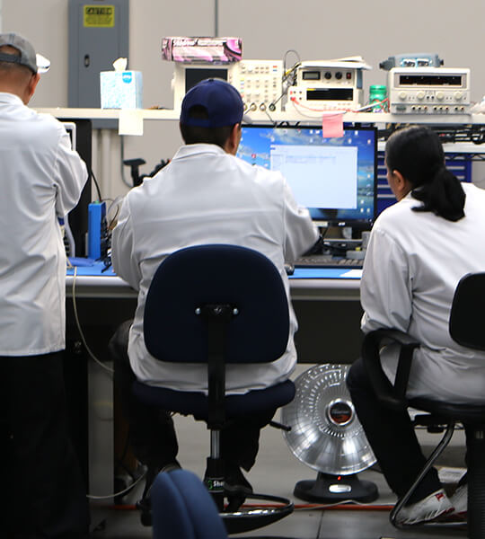 Three people working in lab coats around a computer