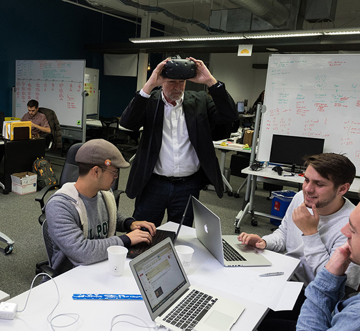 entrepreneurs gather around computers with a mentor wearing a VR headset