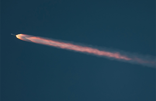 A rocket streaks against a blue sky with a long pink trail