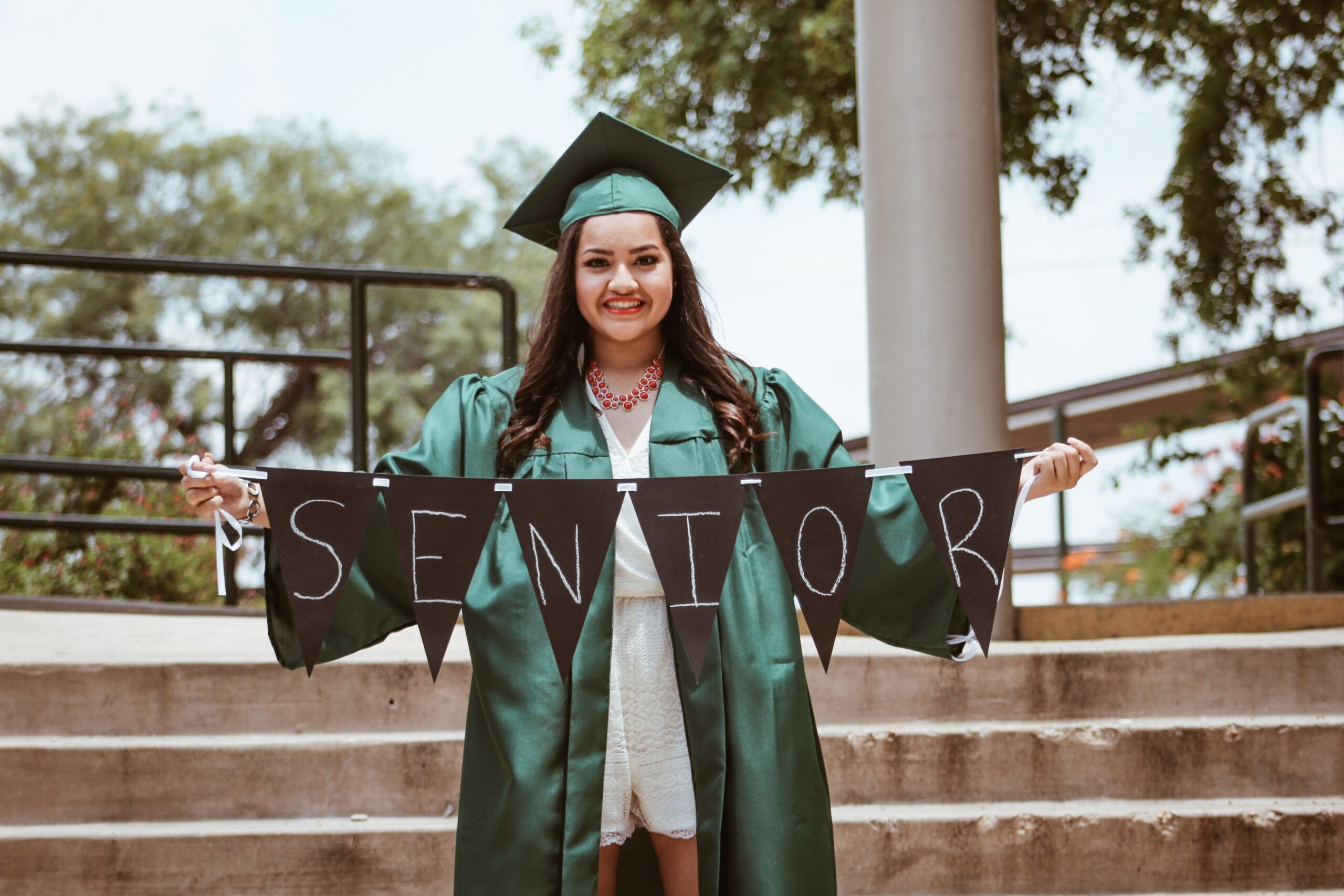 Woman holding a senior sign in a green graduation cap and gown